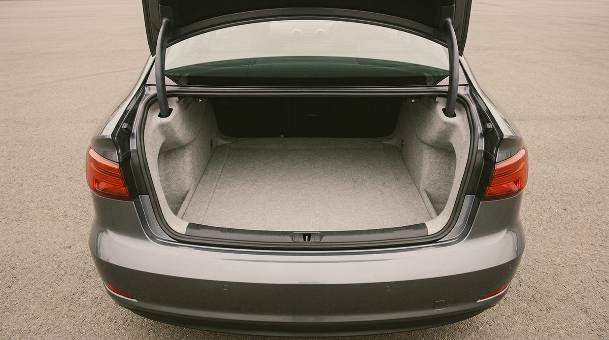 The open, empty luggage compartment of a clean modern dark sedan, photographed square on from behind, with no plate and no maker badge visible